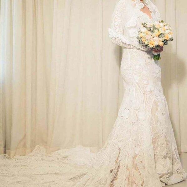 bride wearing a lovely handmade lace wedding dress with long sleeves, a long train and holding gorgeous bouquet
