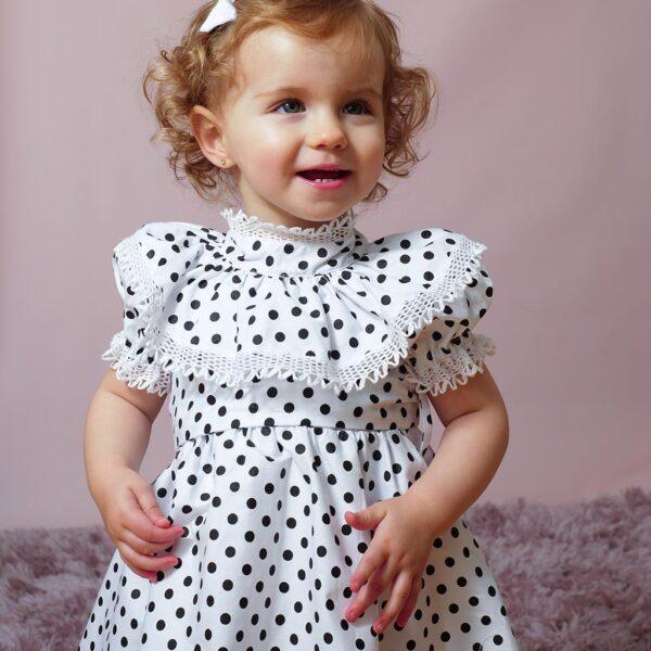 small girl wearing a sweet navy polka dot dress with ruffled collar and sleeves adorned with bobbin lace trims